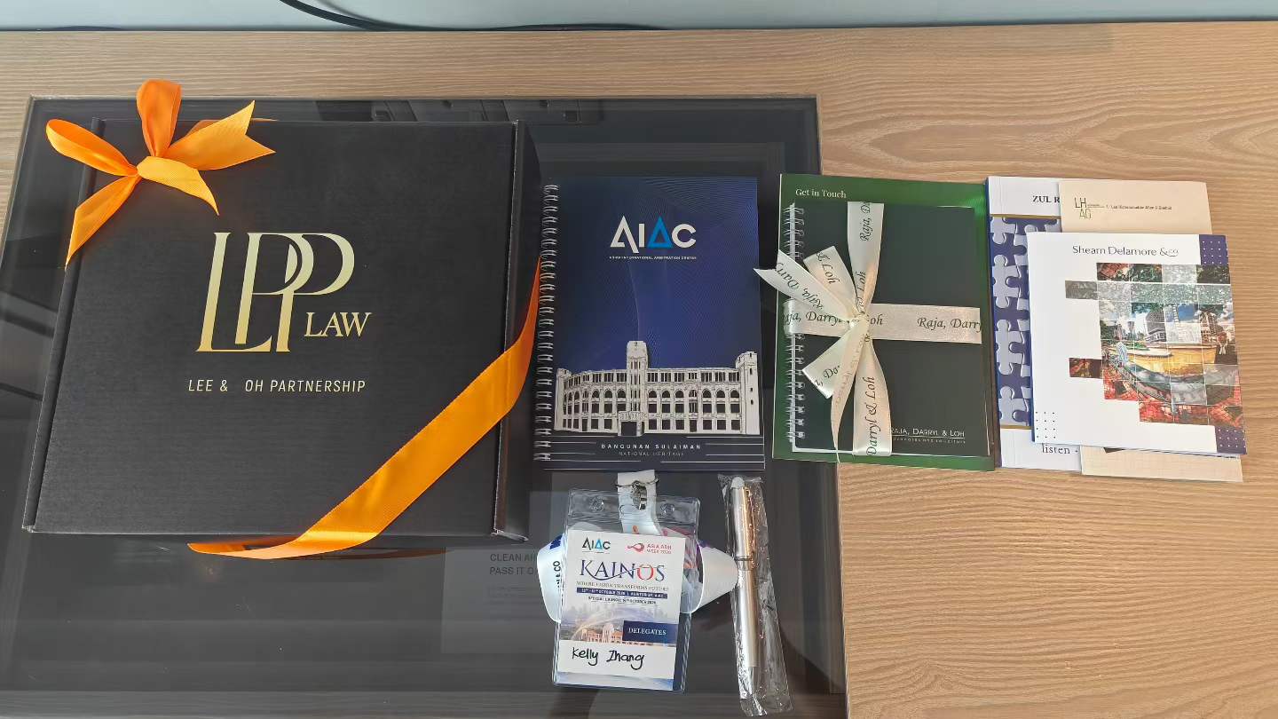 An AIAC KAINOS delegate badge for Kelly Zhang arranged with notebooks and gifts from Malaysian law firms