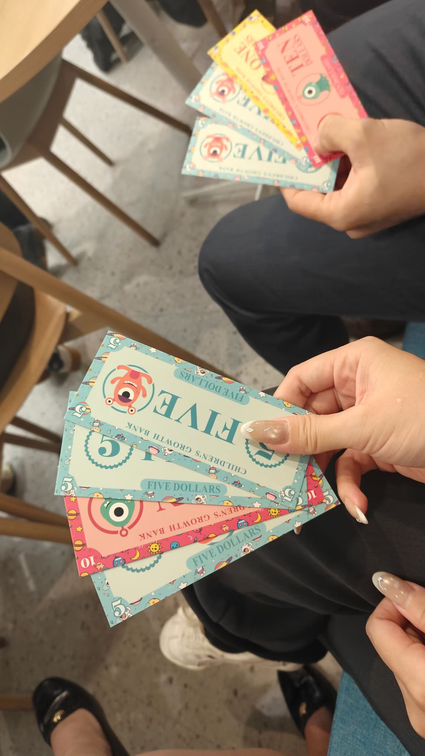 Colourful illustrated play-money notes held in two hands during the JT&N blind-box auction