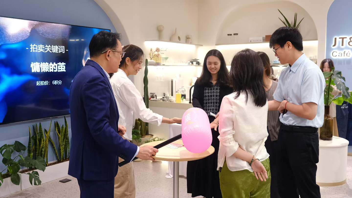 JT&N colleagues gathered around a small table with a pink mystery box during the birthday gathering's blind-box auction