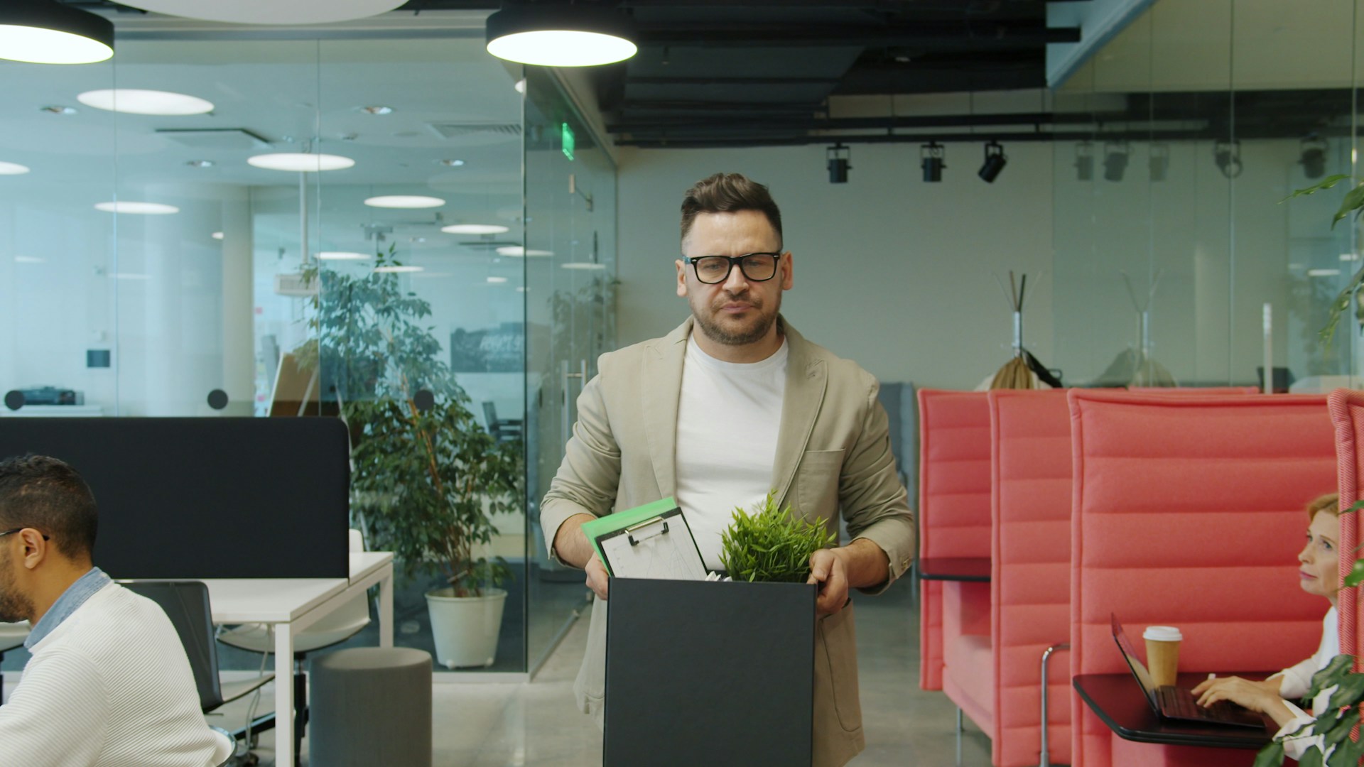 An employee carrying a box of belongings and a desk plant through an open-plan office after being let go